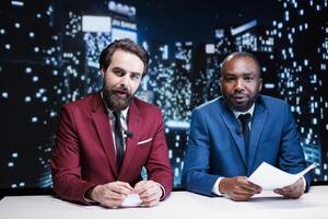 Diverse newscasters team reporting live news in media studio, presenting latest topics for global communications. Journalists working as night show hosts creating fun television content. photo