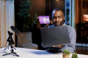 BIPOC content creator filming tech tutorial on how to repair water damaged laptop, presenting internal components. Technology guru in home studio teaching subscribers to install operating system photo
