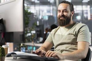 Happy worker looking at PC monitor, satisfied after finding business insights to finish project task. Jolly man smiling while analyzing data on computer, amused by coworker joke photo