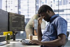 Exhausted man rubbing eyes, working with machine learning tech advancing AI innovating autonomous systems. Tired IT expert in office struggling to stay awake, transforming data into predictive models photo