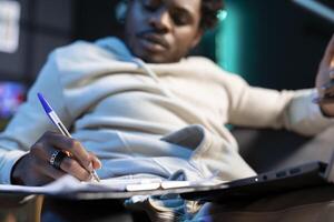 Close up of notepad used by freelancer working from home to write contact details of business partner. Focus on pen and paper used by man in blurry background to note client telephone number photo