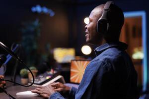 African american man speaking into microphone, broadcasting a radio session for the internet. Black male host interviewing a person in his home studio, making a podcast episode for online audience. photo