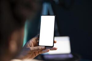 BIPOC man chatting with online friends using mockup phone in warm stylish home, enjoying himself. Person scrolling on isolated screen cellphone, relaxing by scrolling on social media photo