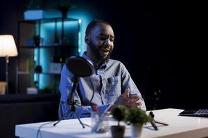 Happy online star in dark room filming reviews of various electronics, unboxing them and presenting features to viewers. Internet show host showcasing product recommendations from personal studio photo