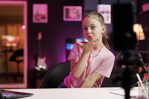 Talented generation Z entertainer doing livestream using cellphone attached to tripod stabilizer. Upbeat youngster does live broadcast using phone camera, sending flying kisses to online subscribers photo