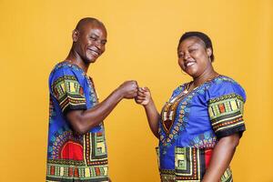 Smiling african american couple making fist bump and looking at camera with cheerful expression. Carefree man and woman showing greeting gesture portrait on orange background photo