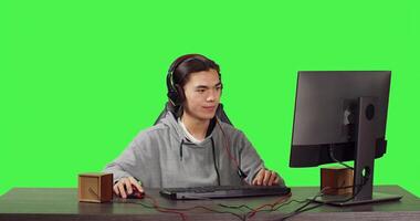 Asian player on computer at pc, playing web videogames with people across the globe. Young person having fun with roleplaying competition, communicating with friends over greenscreen. photo