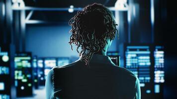 African american woman walking in server room housing advanced infrastructure storing massive datasets, running code on tablet to upgrade data center units doing complex computational operations photo