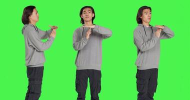 Person does timeout gesture with hands, asking for a break or pause against greenscreen in studio. Asian man showing disapproval and negative emotions on camera, stop gesture. photo