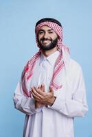 Muslim man wearing traditional clothes displaying support gesture by applauding with hands in studio. Smiling arab clapping arms and looking at camera with excited expression photo