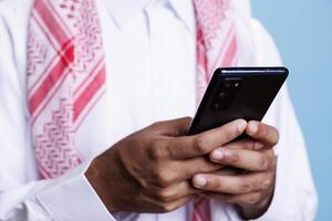 Muslim man hands holding smartphone and typing online message on social media network closeup. Islamic person in traditional clothes using mobile phone, scrolling internet pages photo