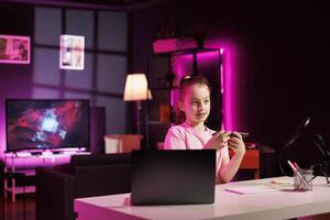 Child media star filming about best smartphones launched this year. Cute girl tech content creator recording mobile phone review, assessing build quality and performance photo