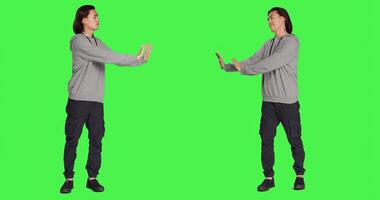 In studio, person tries to shove object aside, presenting rejection or resistance. Against isolated full body greenscreen set, young model resembles refusal and disagreement with stop gesture. photo