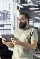 Man working in office developing software in Java programming language using device. Programmer walking through workspace with tablet, thinking how to solve coding problems photo