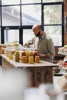 Young man carrying shopping basket while looking at jars of different fresh food products. Male consumer searching for sustainable items with plastic free packaging at local convenience store. photo