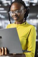 African american woman employee using laptop device to analyze datasets, comparing marketing graphs and checking accounting figures. Young adult with glasses solving tasks for team project on notebook photo
