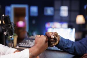 Closeup of host welcoming guest to home studio and preparing to hear thoughts on current events on radio program. Influencer fist bumps and greets individual before beginning podcast. photo