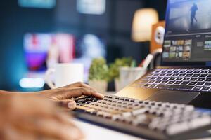 Black person editing and creating digital content using her laptop and keyboard. African american producer multitasking and utilizing editing software on a personal computer. photo
