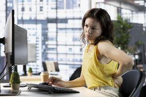 Programmer feeling back pain while sitting at desk testing company software to minimize occurrence of bugs. Fatigued woman suffering pain from incorrect posture while writing code photo