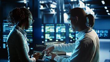 Engineering colleagues running code on tablet and laptop, updating professional data center equipment designed to accommodate server racks, networking gadgets and storage arrays photo