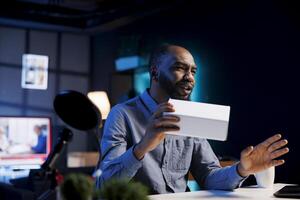 Entertainer at home holding product box in hand, preparing to unbox in after finishing introduction. Trending influencer doing tech item review for viewers, convincing them to buy it photo