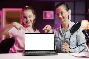 Daughter and mom being sponsored by partnering brand to do mockup laptop unboxing content. Child and parent do influencer marketing, doing isolated screen notebook product placement photo
