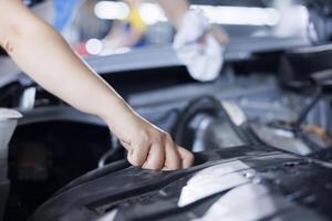 Precise serviceman in garage finishing fixing car, looking underneath vehicle hood to remove remaining oil leaks. Worker does routine alternator cleaning on client automobile in auto repair shop photo