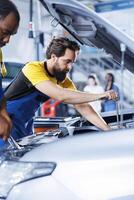 Licensed repairmen in auto repair shop working together on fixing car, discussing best options. Teamworking colleagues collaborating on servicing broken vehicle, checking for faulty engine photo