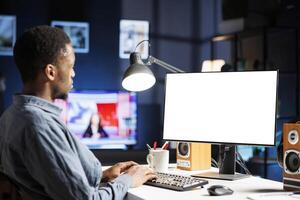 African american guy looks at white screen on monitor, working from home and using empty display on computer. Young employee does remote work with isolated copyspace layout. photo