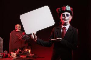 Smiling woman holding speech bubble during Day of the Dead Mexican event honoring dead loved ones. Person using isolated copyspace template, promoting ancient Aztec custom of celebrating ancestors photo