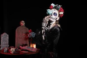 Woman with eyes closed posing with flower for Day of the Dead event to remember the deceased, celebrating their memory. Girl holding blue rose for holiday of remembrance for those who have passed photo