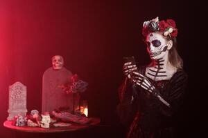 Woman holding mobile phone at Day of the Dead event to remember the deceased, celebrating their memory. Lady texting on smartphone during Mexican holiday of remembrance for those who have passed photo