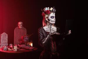 Woman working on laptop during Day of the Dead Mexican event honoring dead loved ones. Person sending emails on notebook during Halloween ancient Aztec custom of celebrating ancestors event in office photo