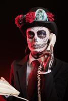 Woman talks on cord telephone during Dia de los Muertes indigenous rites of honoring the dead. Lady uses landline phone to answer call, participating in Day of the Dead event in honor of the deceased photo