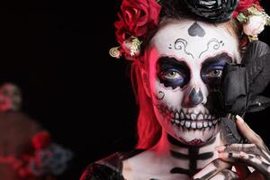 Headshot portrait of woman holding black rose set against dark background celebrating Dia de los Muertos holiday. Close up of lady with flower during Halloween horror event photo