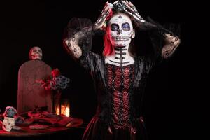 Portrait of person at religious processions during Dia de los Muertos. Woman wearing skull makeup and floral crown symbolizing reverence for the deceased, dark studio background photo