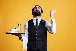 Skilled waiter praying to god for success, asking for good fortune and being spiritual. Faithful religious person working as butler with food tray and formal attire, feeling optimistic in studio. photo
