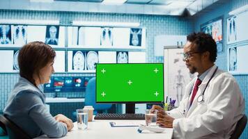 General practitioner consulting a female patient next to isolated chroma key display, sharing insight on lab test results and analysis. Skilled medic supports his client, indoors check up. Camera B. photo
