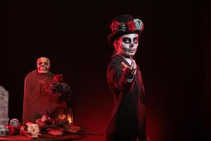 Portrait of woman doing enticing hand invitation in graveyard during Day of the Dead. Mysterious lady does provocative luring gesturing, surrounded by frightening funeral items during Halloween event photo