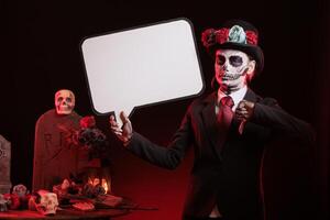 Woman using isolated copyspace template, doing negative gesturing at Day of the Dead event. Lady holding speech bubble and doing thumbs down hand gesture during Mexican holiday of remembrance photo