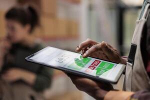 Small business manager supervising goods inventory using software application on tablet computer in storage room. Storehouse supervisor managing parcels transportation. Close up concept photo