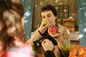 Selective focus of vendor smelling freshly harvested vibrant apples, helping client in selecting best product. Female supplier browsing locally grown bio produce, choosing for customer. photo