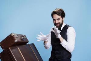 Happy hotel porter in suit posing on camera, feeling confident while he dances and acts groovy in studio. Professional elegant bellboy fooling around with silly dance moves. photo
