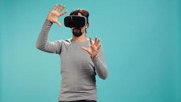 Man wearing virtual reality headset, interacting with interface, doing swiping motions. Person having fun using high tech futuristic modern VR gadget, isolated over blue studio background, camera B photo