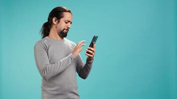 Man scrolling on smartphone touchscreen, using mobile phone to check social media feed, studio backdrop. Person browsing internet websites, isolated over studio background, camera B photo