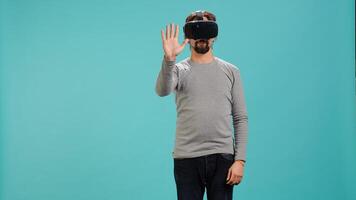 Tech enthusiast wearing virtual reality goggles, doing zooming in gestures. Arab man using high tech futuristic modern VR glasses, making tactile touching gesturing, studio background, camera A photo