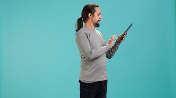 Jolly man excited to greet friends during teleconference meeting using tablet, studio background. Merry person waving hand, saluting mate during internet call on portable device, camera A photo