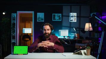 Tech specialist presenting mockup tablet to interested viewers, filming with professional mic. Man reviewing green screen digital device, recording with specialized equipment, camera B photo