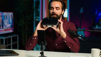 Media star in neon lit studio presents VR goggles from brand sponsoring , closely analyzing features. Influencer reviewing virtual reality headset for tech enthusiasts watching, camera A photo