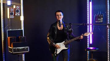 Woman rocker dressed in leather performs a live show with heavy metal tunes, music lover vocal performance. Rebellious edgy singer plays guitar with a wild stage presence. Camera B. photo